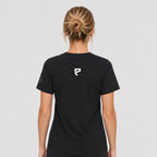St. Padel Lifestyle Cotton T-Shirt. A woman viewed from the back wearing a black short-sleeve t-shirt with a small white stylized ST PADEL logo centered on the upper back, against a light gray studio background.
