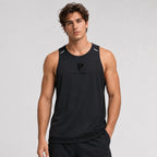 St_Padel Men's Performance Tank Top. A man wearing a black sleeveless athletic tank top with a small black logo on the chest, paired with black shorts, photographed against a light gray studio background.