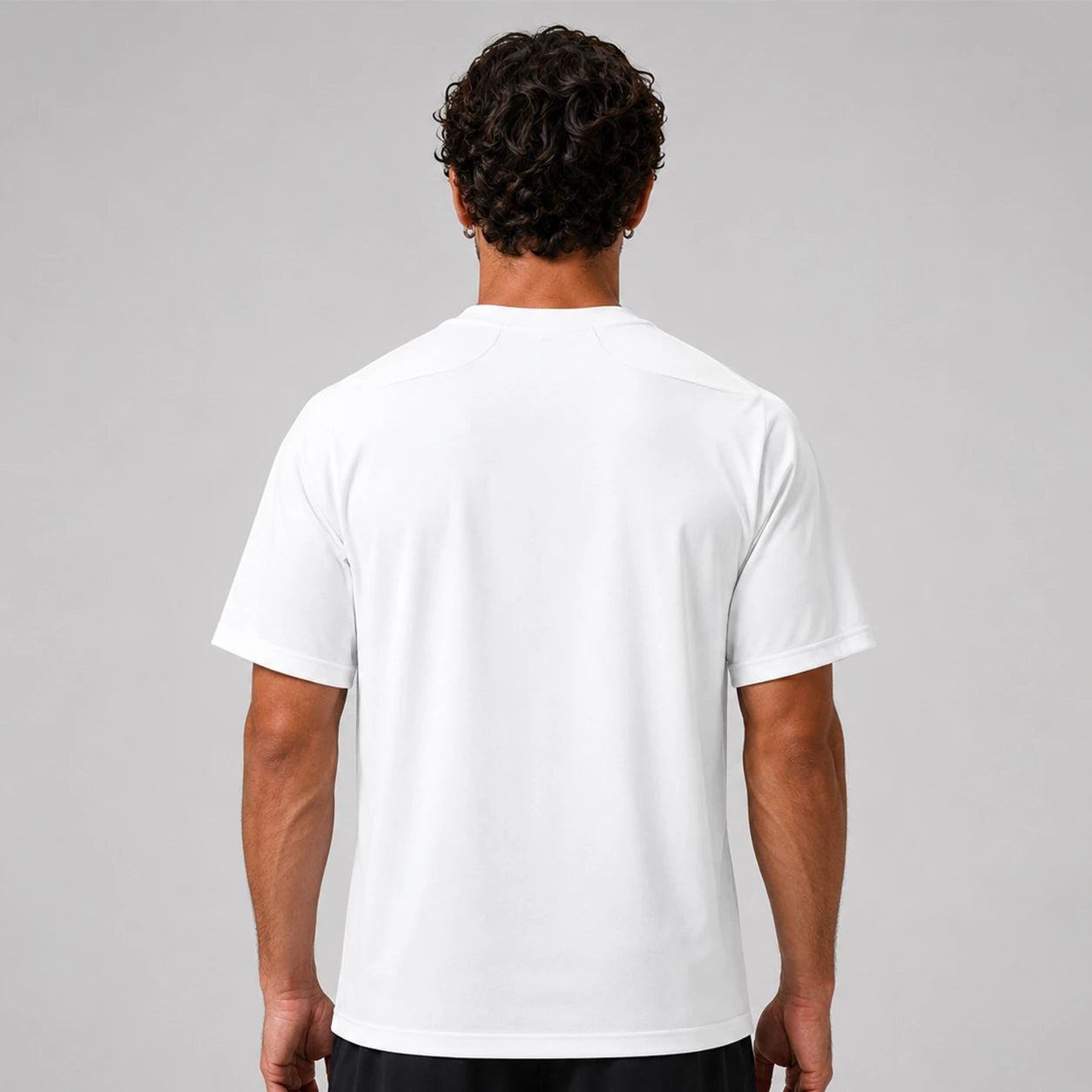 St. Padel Performance Padel T-Shirt. A man viewed from behind wearing a plain white short-sleeve athletic T-shirt against a light gray studio background.