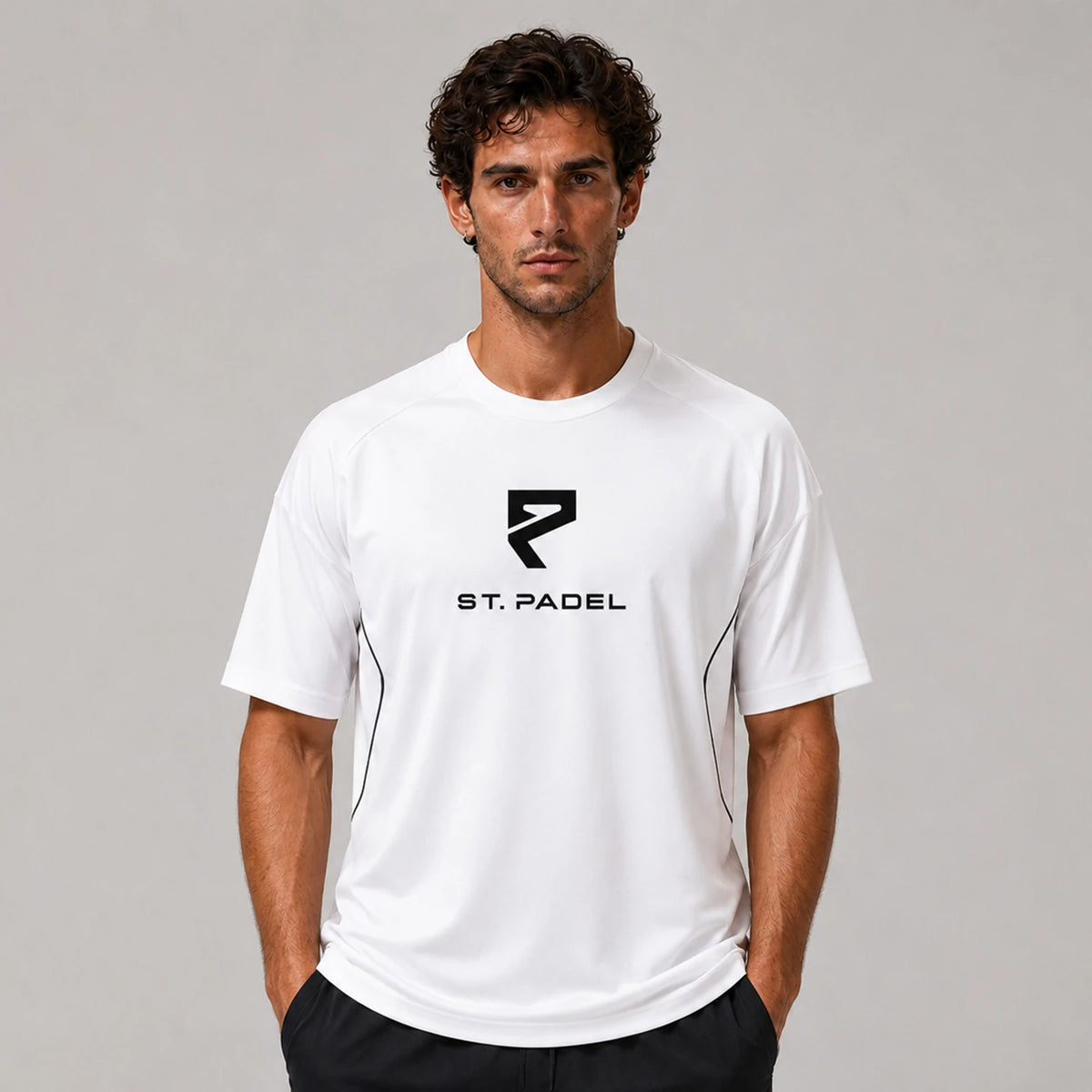 St. Padel Performance Padel T-Shirt. A man wearing a white short-sleeve athletic t-shirt with a black St. Padel logo on the chest, standing against a neutral gray studio background.