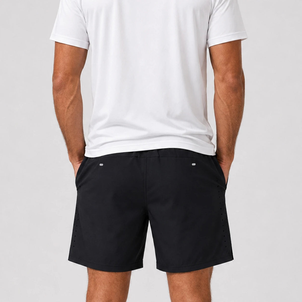 St Padel Performance Shorts. A man wearing black athletic shorts and a white t-shirt, shown from the back against a light gray studio background.