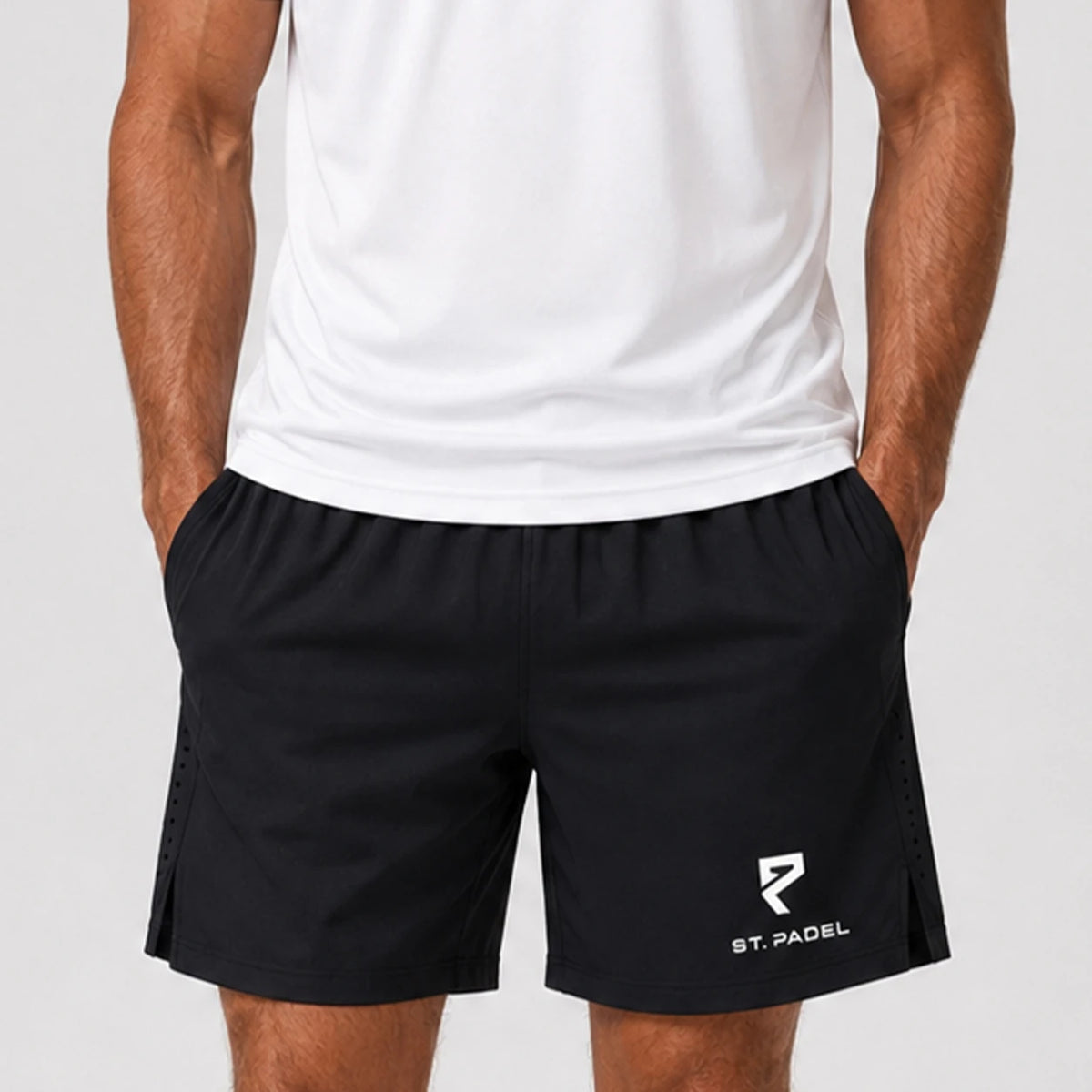 St Padel Performance Shorts. A man wearing black athletic shorts with a white St. Padel logo on the lower left leg, paired with a white sleeveless top, shown from the chest down against a light gray background.