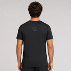 St. Padel Performance T-Shirt. A man viewed from behind wearing a black short-sleeve t-shirt with a small circular logo on the upper back, set against a plain light gray studio background.