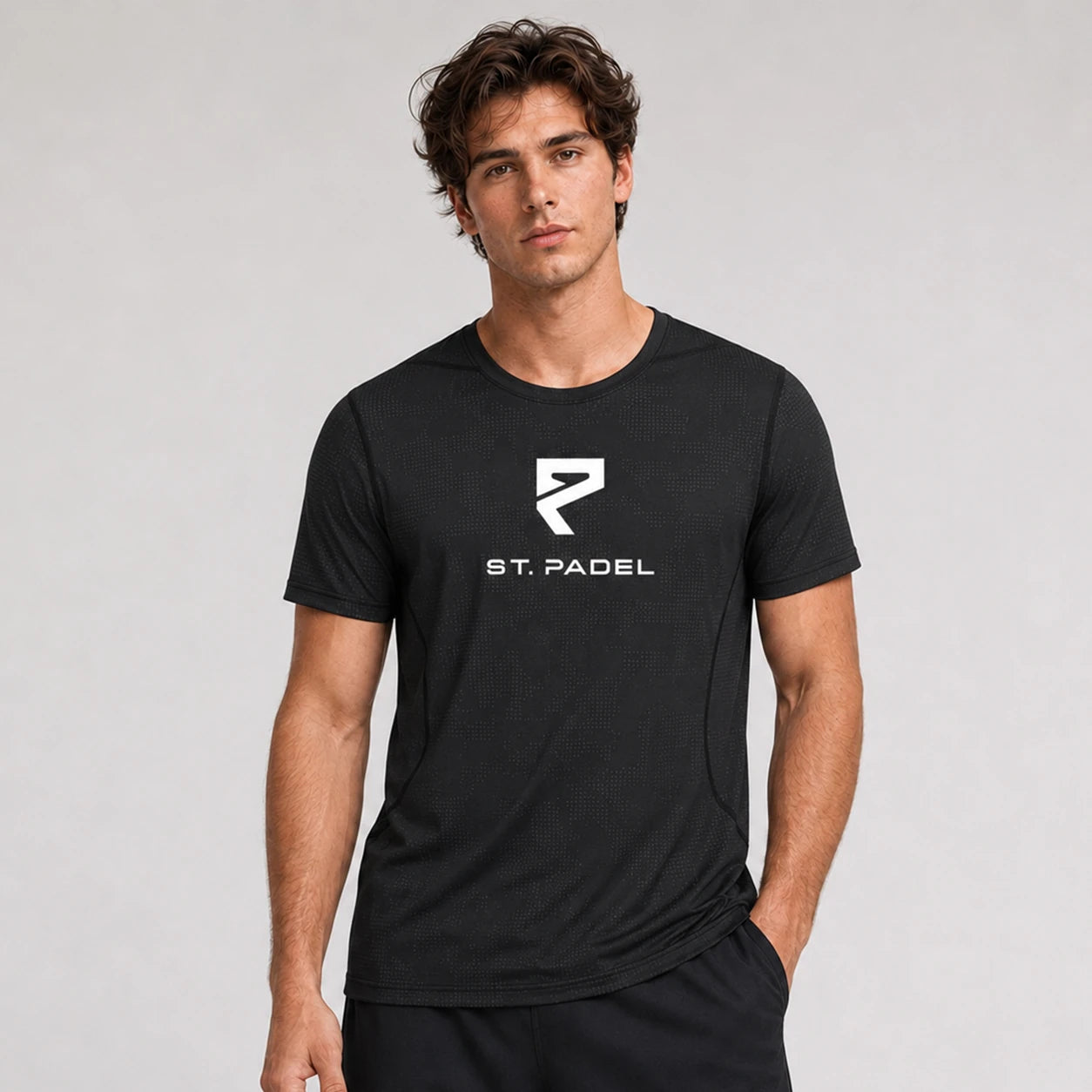 St. Padel Performance T-Shirt. A man wearing a black short-sleeve athletic t-shirt with a white St. Padel logo and text on the chest, photographed against a light gray studio background.