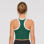 St. Padel Performance Tank. A woman viewed from behind wearing a dark green athletic crop top with white trim on the neckline and racerback straps, paired with black bottoms, against a light gray studio background.