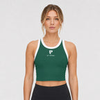 St. Padel Performance Tank. A woman modeling a dark green cropped tank top with white trim and a white ST. PADEL logo on the chest, paired with black leggings, against a light gray studio background.