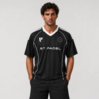 St Padel Shadow Stripe Jersey. A man modeling a black short-sleeve soccer jersey with white accents, featuring the text 'ST. PADEL' across the chest and a circular club crest on the left chest, set against a plain light gray background.