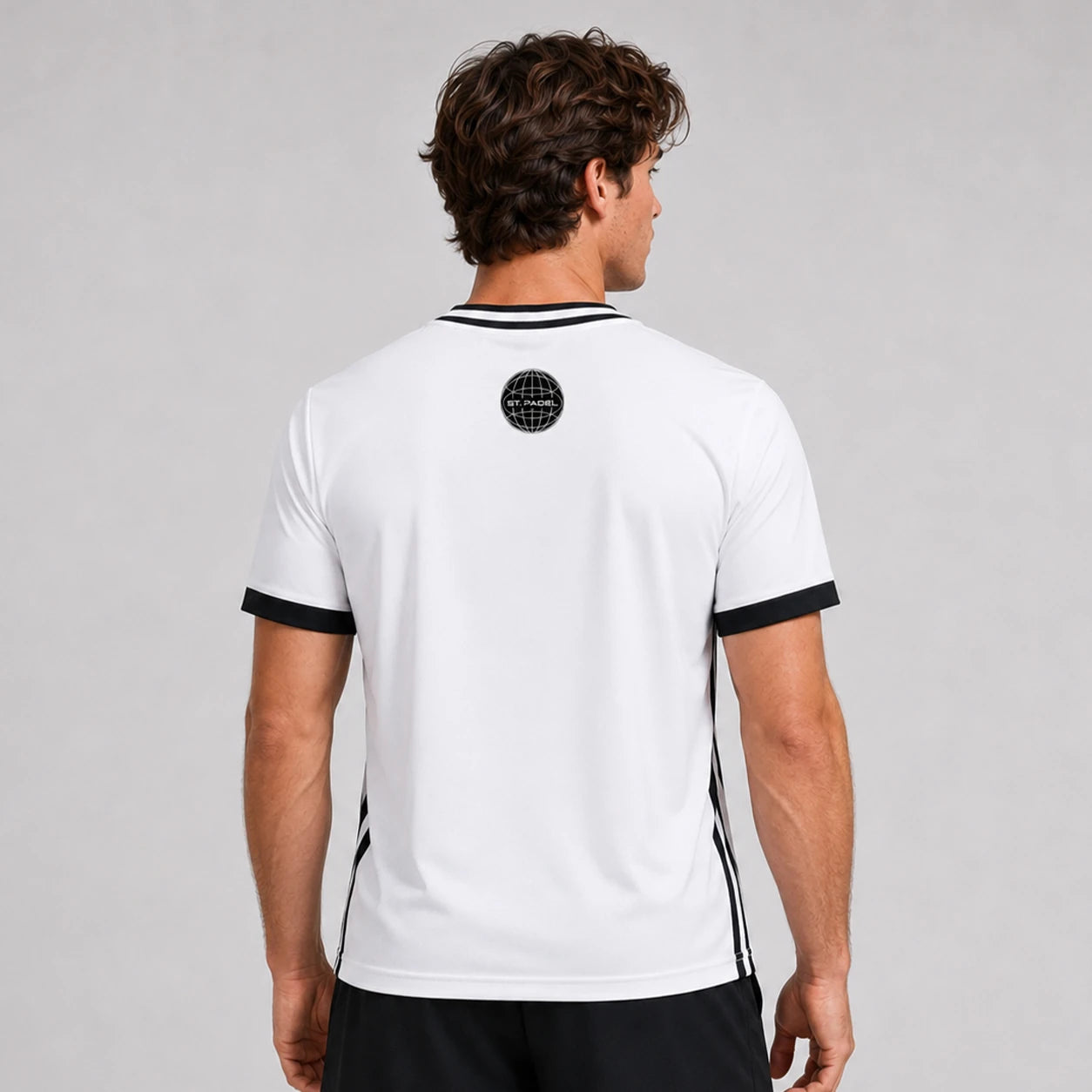 St. Padel V-Neck Jersey. A man viewed from the back wearing a white short-sleeve athletic jersey with black trim at the collar and sleeve cuffs, plus black side stripes and a circular black logo near the upper back.